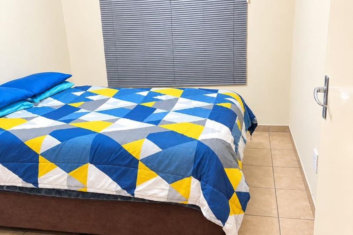 A functional bedroom featuring neutral wall tones, tiled flooring, and a window fitted with grey venetian blinds.