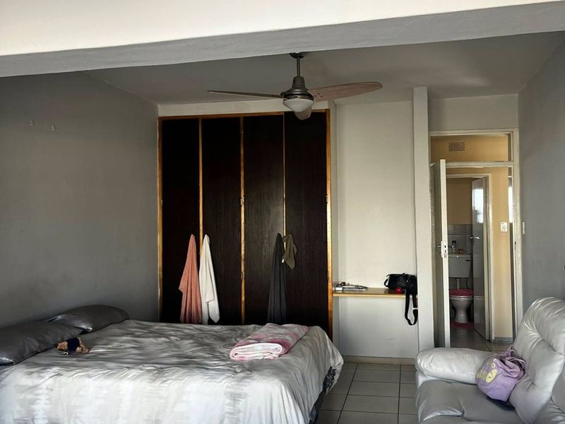 Spacious bedroom featuring built-in cupboards, tiled flooring, a ceiling fan, and direct access to an en-suite bathroom.