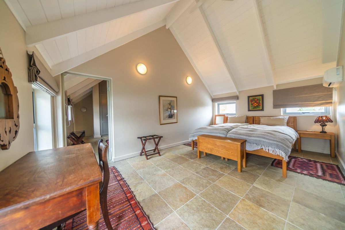 Spacious bedroom featuring a high vaulted ceiling, stone tile flooring, and a wall-mounted air conditioning unit, offering a bright and comfortable living space.