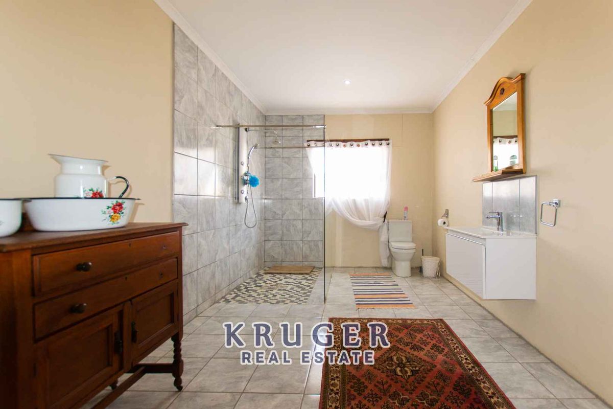 A spacious bathroom featuring a large walk-in shower with glass enclosure, tiled flooring, a wall-mounted vanity, and a toilet.