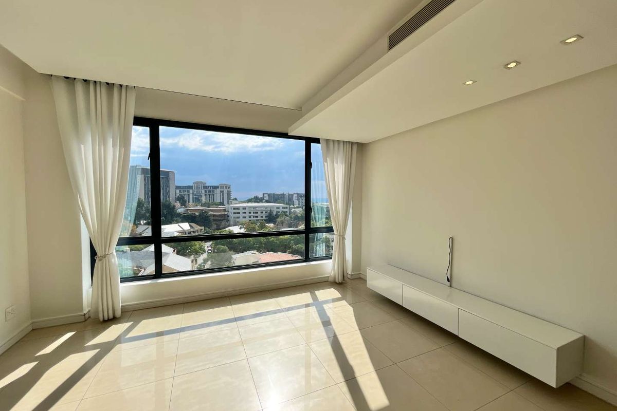A bright and spacious living area featuring large floor-to-ceiling windows with city views, tiled flooring, and a built-in wall-mounted media console.