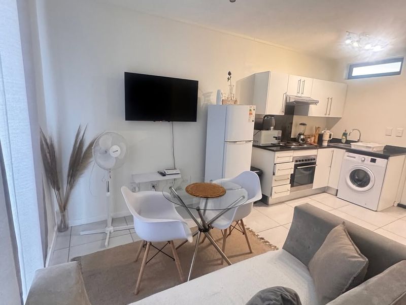 Open-plan living and kitchen area featuring tiled flooring, modern white cabinetry, integrated oven, and track lighting, creating a functional and compact living space.