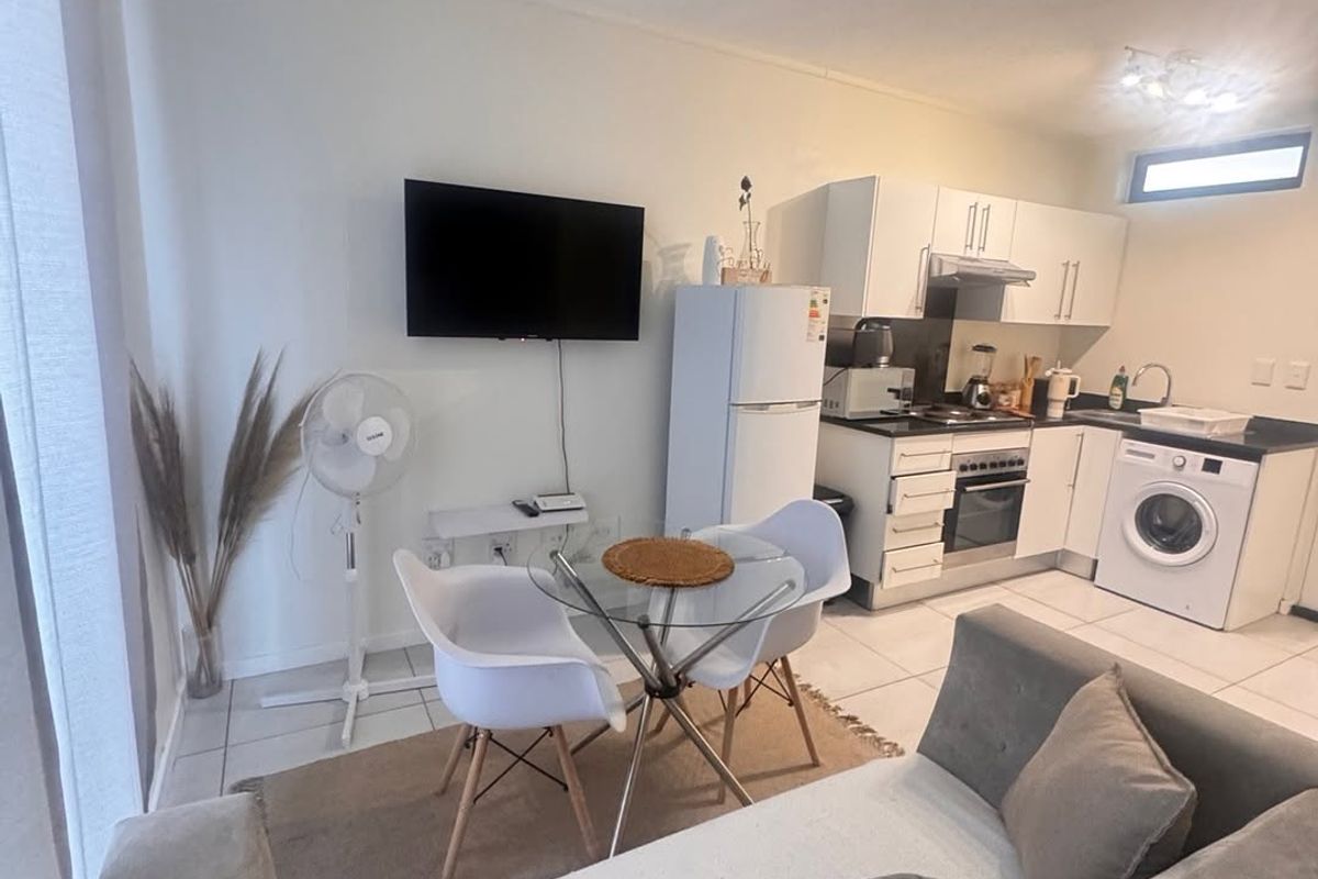 Open-plan living and kitchen area featuring tiled flooring, modern white cabinetry, integrated oven, and track lighting, creating a functional and compact living space.