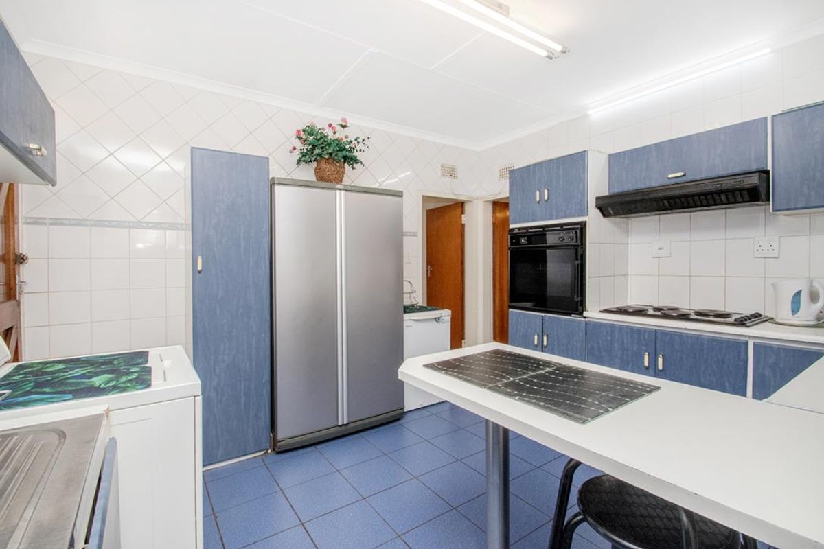 A functional kitchen featuring blue cabinetry, built-in oven, hob, extractor fan, and tiled flooring with a breakfast counter.