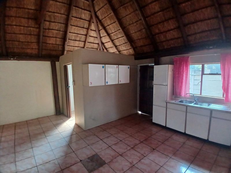 Open plan living area featuring a traditional thatched roof with exposed timber beams, tiled flooring, and a functional kitchen area with built-in cabinetry.