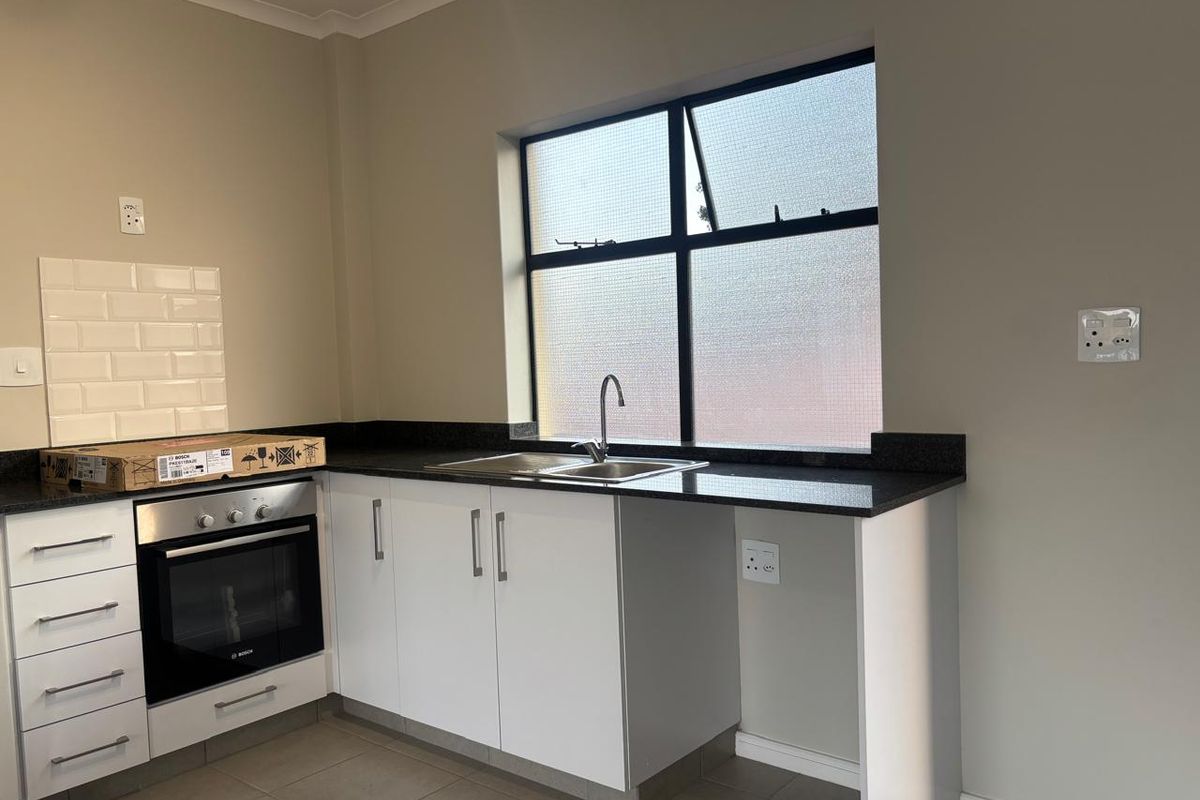 A clean, modern kitchen featuring white cabinetry, granite countertops, a built-in oven, and a subway tile backsplash with ample natural light.