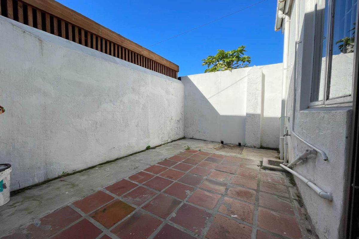 A private rear courtyard featuring terracotta tiling, high boundary walls with timber screening, and external plumbing access.