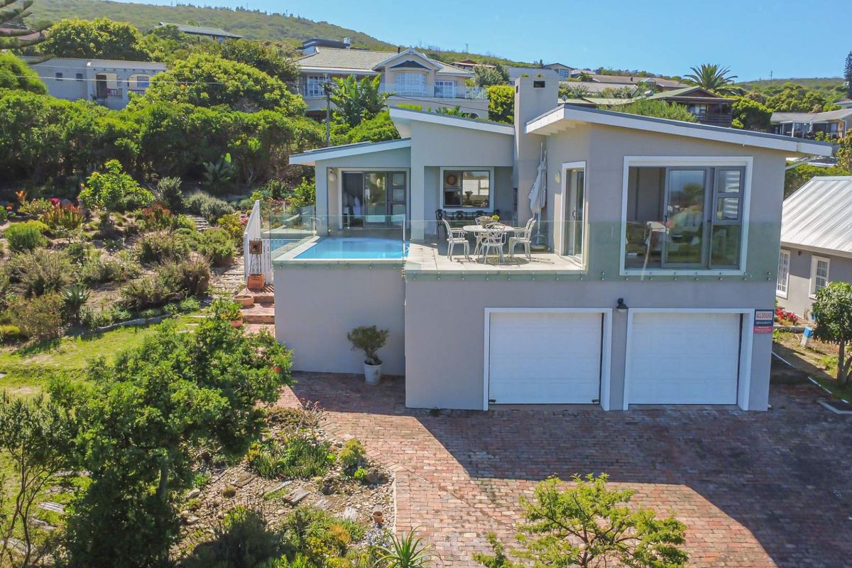 Aerial view of a modern multi-level home featuring a swimming pool, elevated patio, double garage, and landscaped garden in a scenic hillside setting.