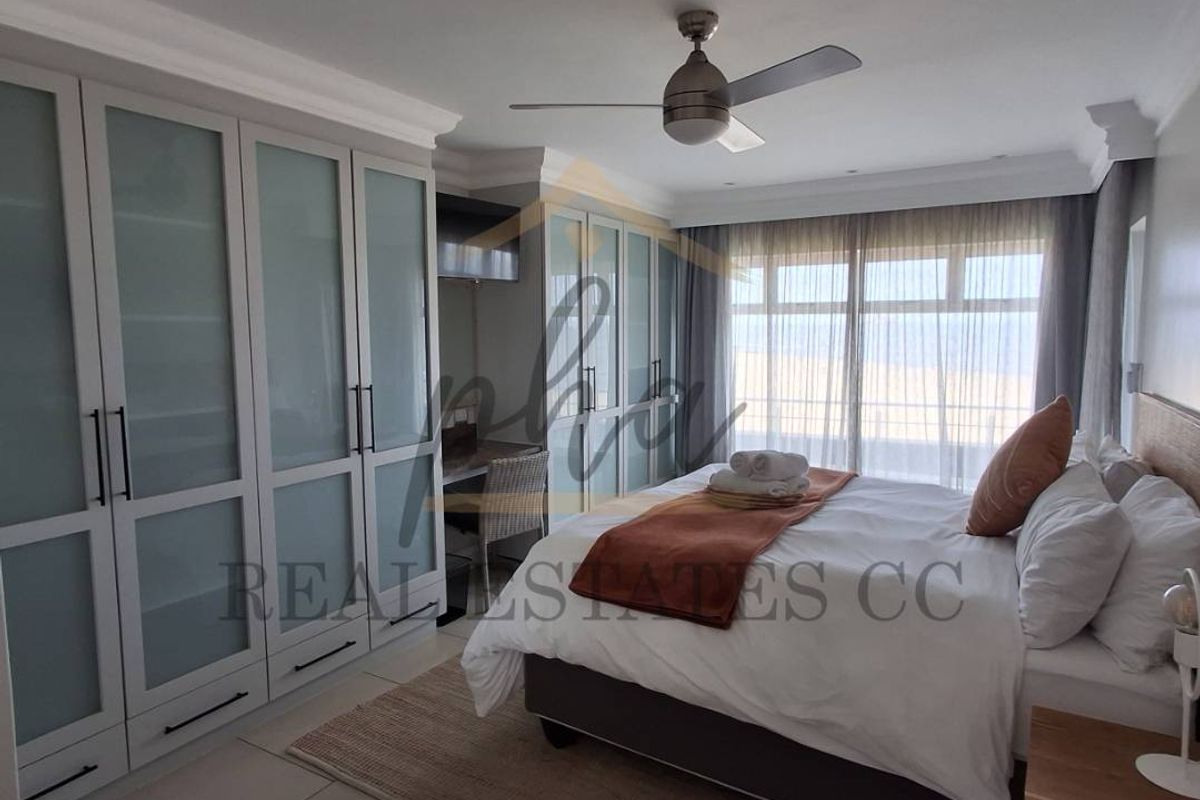 Spacious bedroom featuring extensive built-in cupboards, tiled flooring, a ceiling fan, and large sliding doors providing natural light.