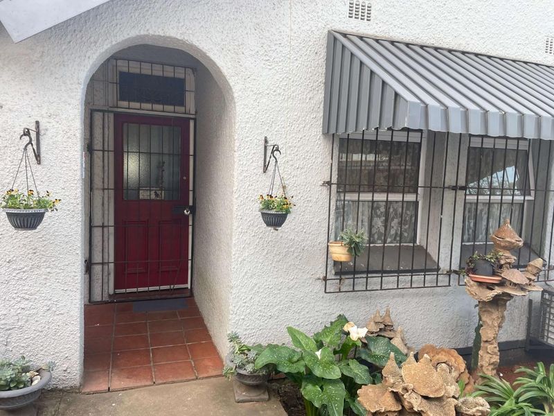 Front entrance featuring an arched doorway with a security gate, tiled porch, and metal window awning with security bars.
