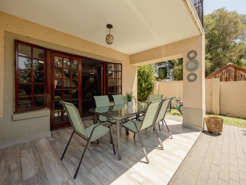 A covered patio area featuring tiled flooring and wooden framed glass doors, providing a seamless transition to the outdoor garden space.