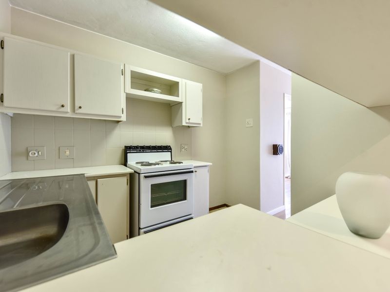 A functional kitchen featuring white cabinetry, a stainless steel sink, and a freestanding stove with a tiled backsplash.