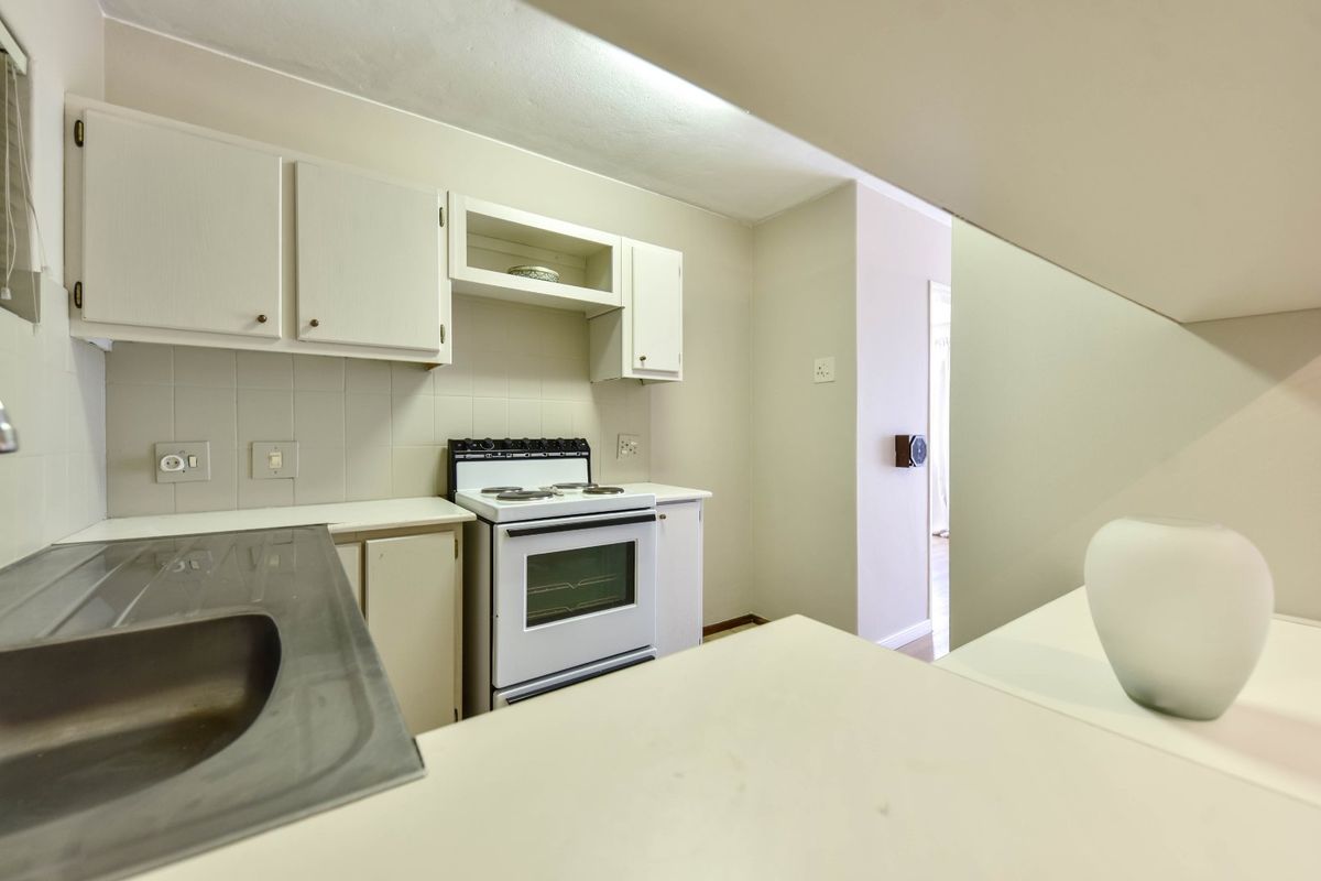 A functional kitchen featuring white cabinetry, a stainless steel sink, and a freestanding stove with a tiled backsplash.