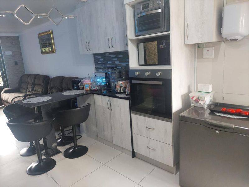 Open-plan kitchen and living area featuring modern cabinetry, built-in oven and microwave, breakfast bar, and tiled flooring.