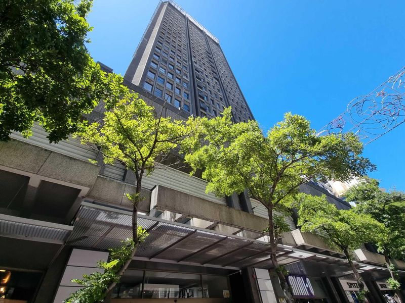 Low angle view of a high-rise apartment building facade featuring a metal entrance canopy and ground-level commercial storefronts.