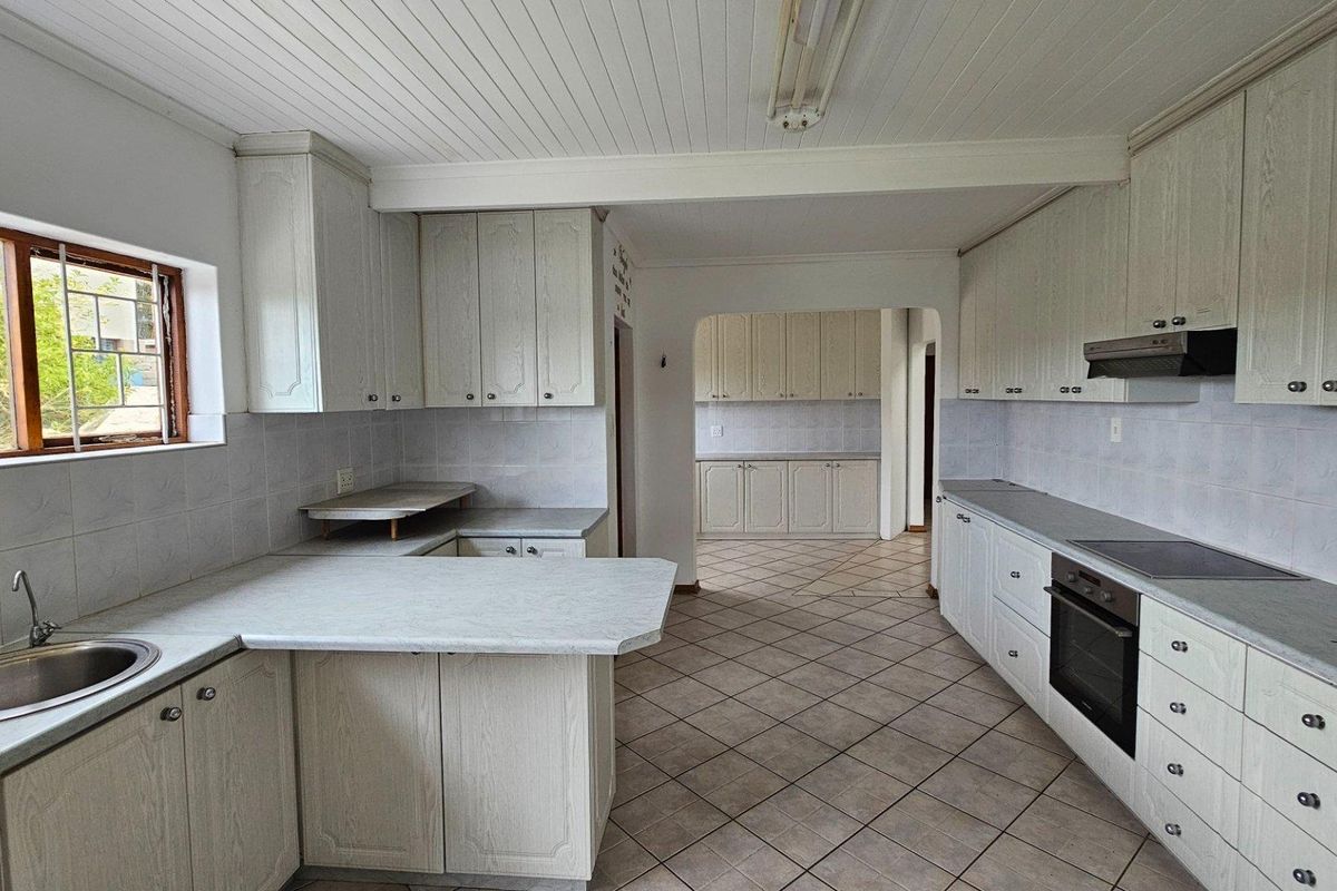 Spacious kitchen featuring extensive cabinetry, built-in oven, hob, extractor fan, and tiled flooring, with an adjoining scullery area.