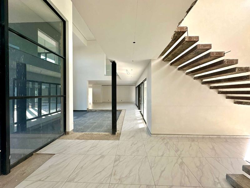 Spacious open-plan interior featuring a modern floating staircase, large format marble-look floor tiles, and expansive black steel-framed glass partitions in an unfinished state.