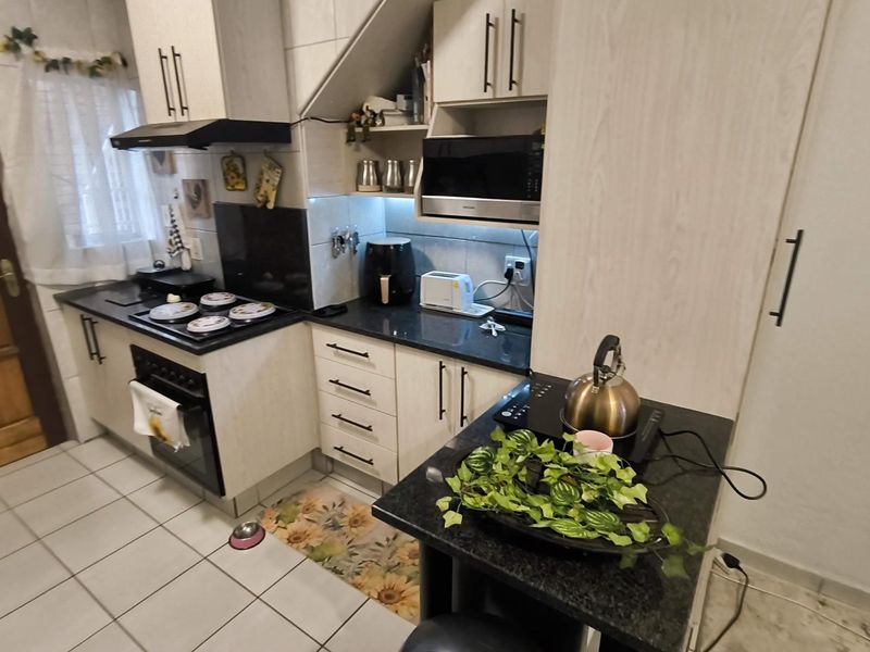 A functional kitchen featuring light-toned cabinetry, dark granite countertops, built-in oven, hob, and extractor fan, complemented by tiled flooring.
