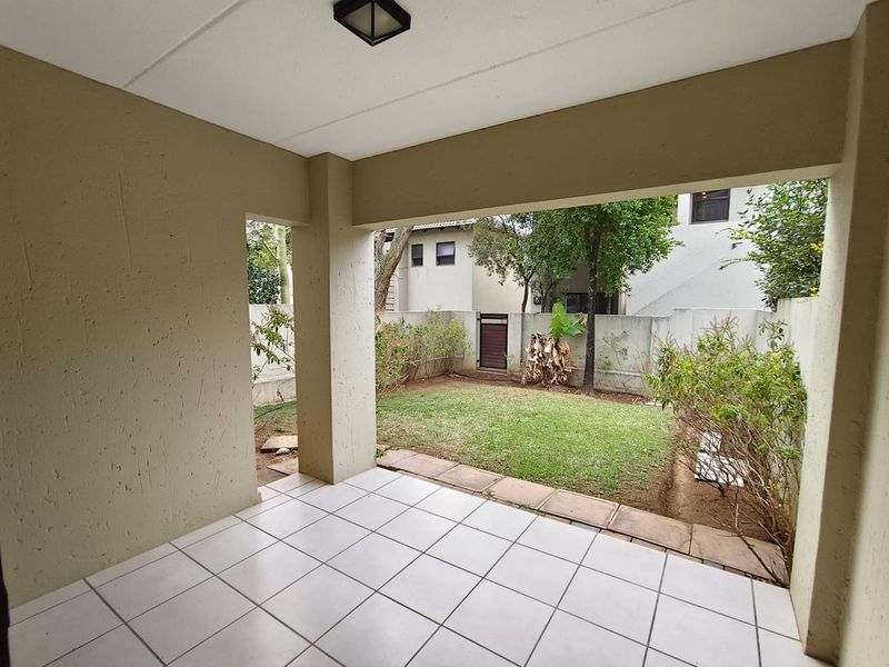 A covered patio area with tiled flooring overlooking a private garden space, enclosed by boundary walls.