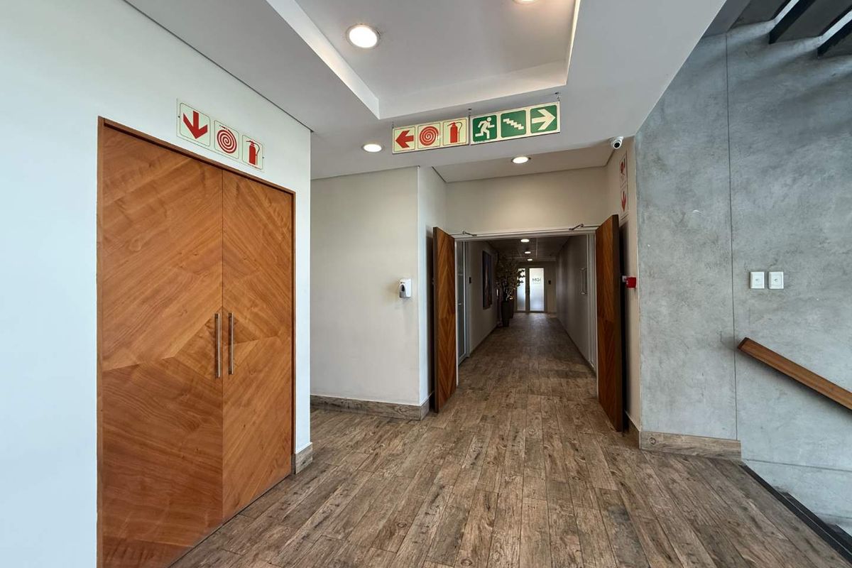 A modern, well-maintained office hallway featuring wood-look tile flooring, recessed lighting, and a striking exposed concrete wall accent.