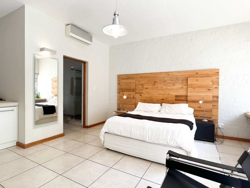 A well-maintained bedroom featuring tiled floors, a custom wooden headboard, integrated desk space, and an en-suite bathroom with air conditioning.