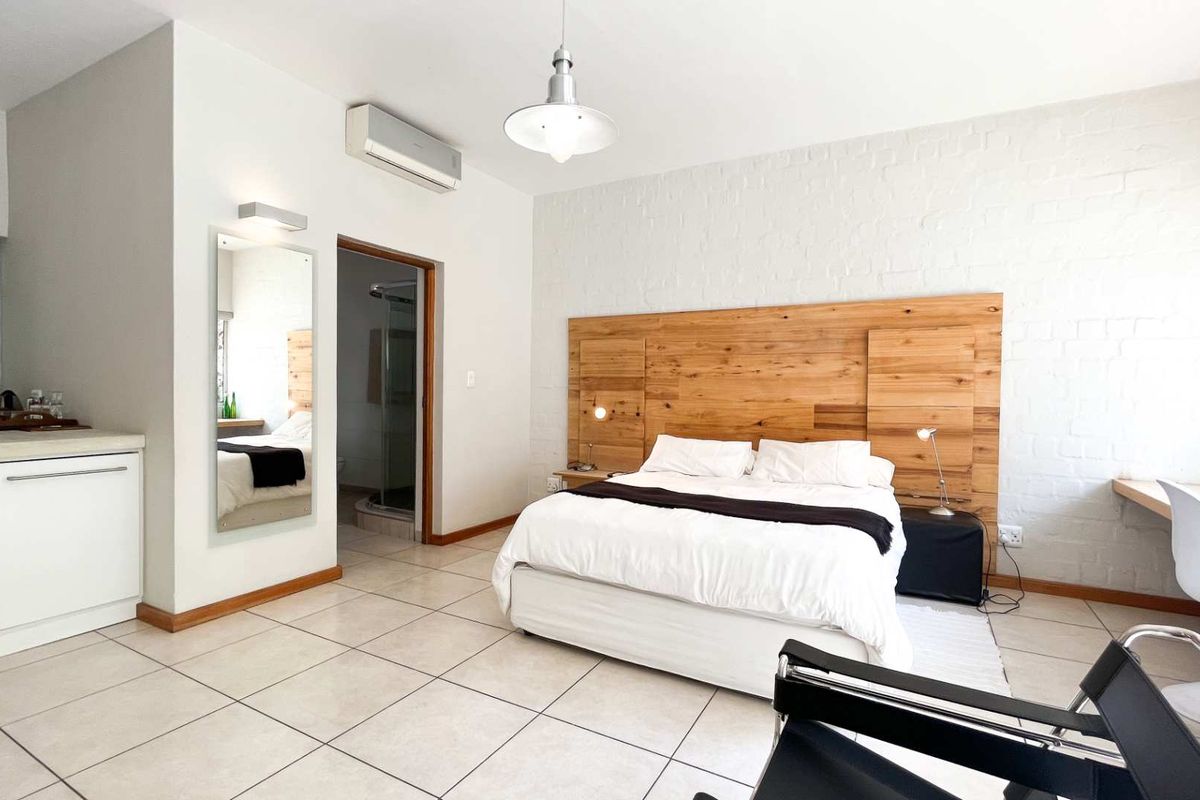 A well-maintained bedroom featuring tiled floors, a custom wooden headboard, integrated desk space, and an en-suite bathroom with air conditioning.