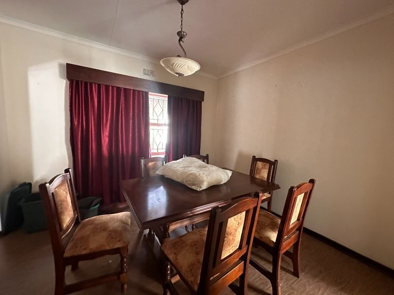 A dining room featuring laminate flooring, a central light fixture, and a window with security bars and a decorative pelmet.