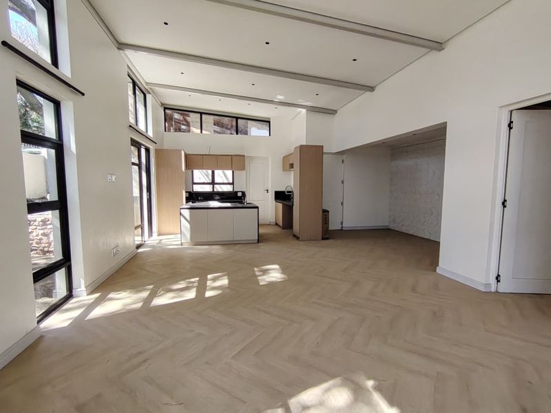 Spacious open-plan living area featuring modern herringbone timber flooring, high ceilings with exposed beams, and a contemporary kitchen with a central island.