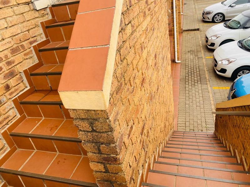 An exterior view of a brick staircase with tiled steps and a metal handrail leading down to a paved parking area.