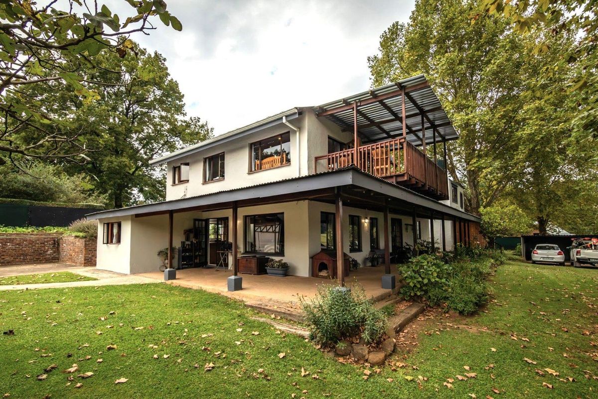 Rear view of a two-story small holding residence featuring a spacious ground-floor covered patio and an elevated timber balcony with a corrugated metal roof.
