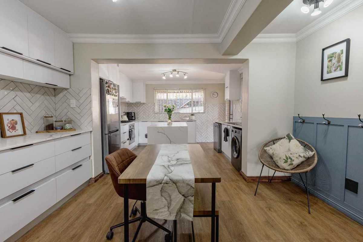 Modern kitchen featuring white cabinetry, herringbone tile backsplash, quartz countertops, and integrated appliances, seamlessly flowing into a dining area with wood-look flooring.