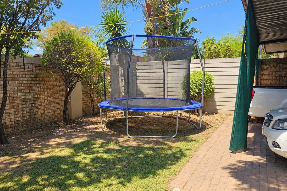A private rear garden area featuring a brick boundary wall, paved driveway section, and a covered carport structure.