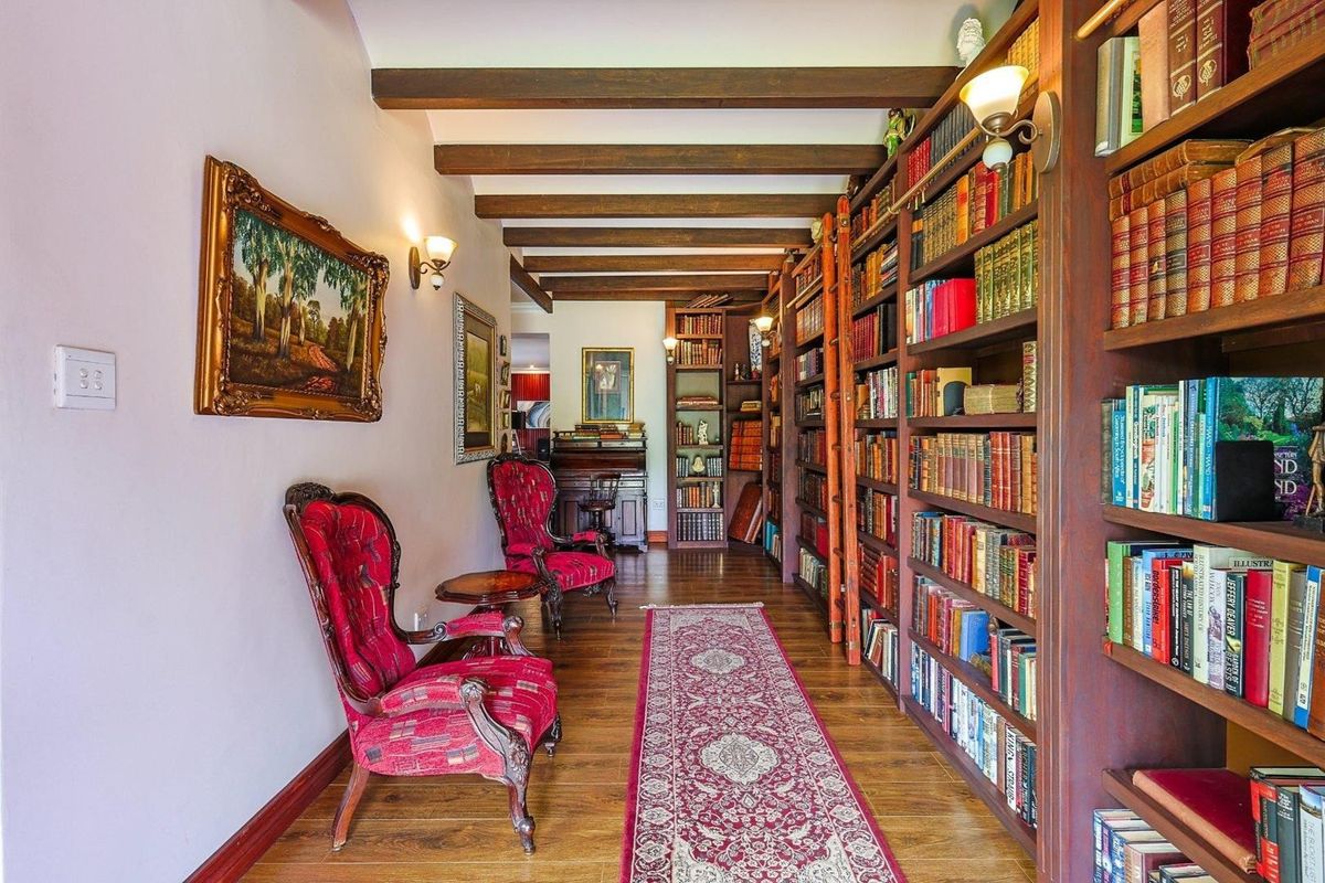 A cozy library or study area featuring extensive floor-to-ceiling built-in wooden bookshelves, exposed timber ceiling beams, and warm hardwood flooring.