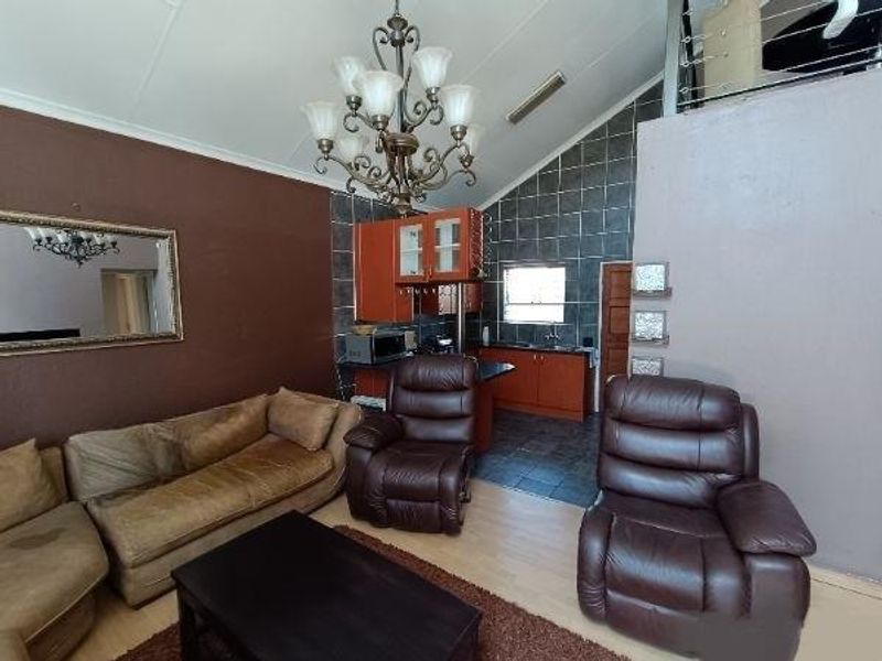 Open-plan living area featuring a vaulted ceiling, chandelier, and an integrated kitchen with tiled backsplash and cabinetry, leading to a mezzanine level.