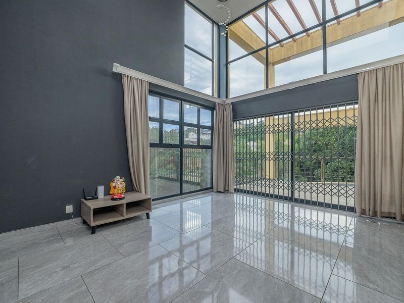 Spacious double-volume living area featuring large windows, tiled flooring, and direct access to an outdoor patio area with a pergola.