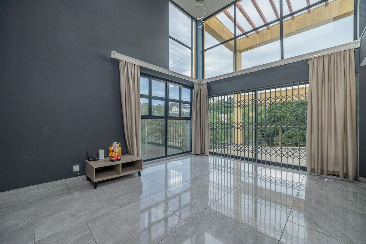 Spacious double-volume living area featuring large windows, tiled flooring, and direct access to an outdoor patio area with a pergola.