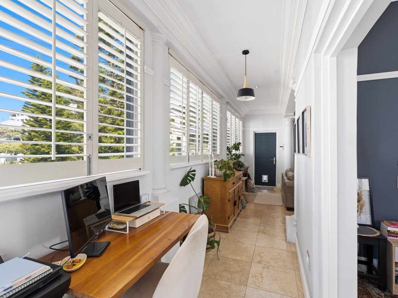 A bright and spacious hallway featuring elegant plantation shutters, stone tile flooring, and decorative crown molding, creating a welcoming transition between living areas.