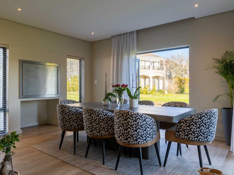 A bright and modern dining room featuring laminate flooring, recessed downlights, and a built-in braai, with large windows overlooking the garden.