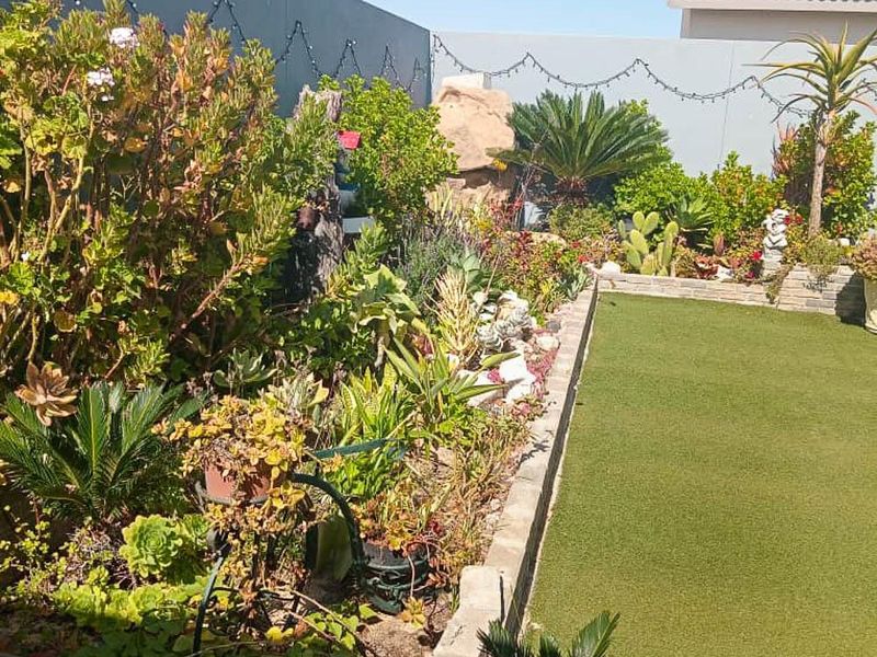 A well-maintained rear garden featuring artificial turf, established garden beds with diverse plantings, and a solid perimeter wall with decorative string lighting.