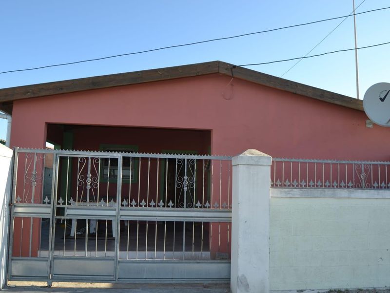 Front elevation of a residential property featuring a metal security gate, masonry boundary wall, and a covered porch area.