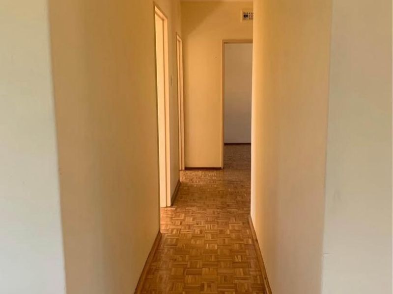A clean, empty hallway featuring classic parquet wood flooring and neutral wall finishes, providing access to multiple rooms within the apartment.