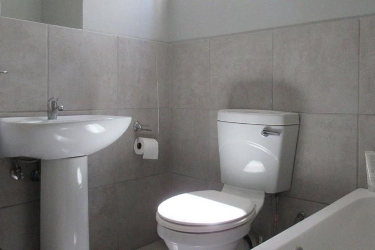A functional bathroom featuring a pedestal sink, a standard toilet, and a bathtub with neutral wall tiling.