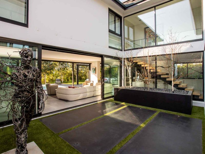 Modern central courtyard patio featuring large sliding glass doors, integrated planter box, and a view through to the open-plan living area and staircase.