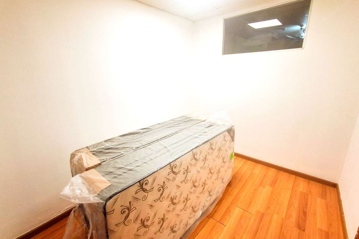 A compact bedroom featuring wood-look laminate flooring and a high-set horizontal window, providing a clean and neutral space ready for personalization.