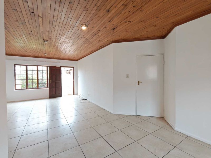 Spacious living area featuring ceramic floor tiles, a warm timber tongue and groove ceiling, and natural light through wooden window and door frames.