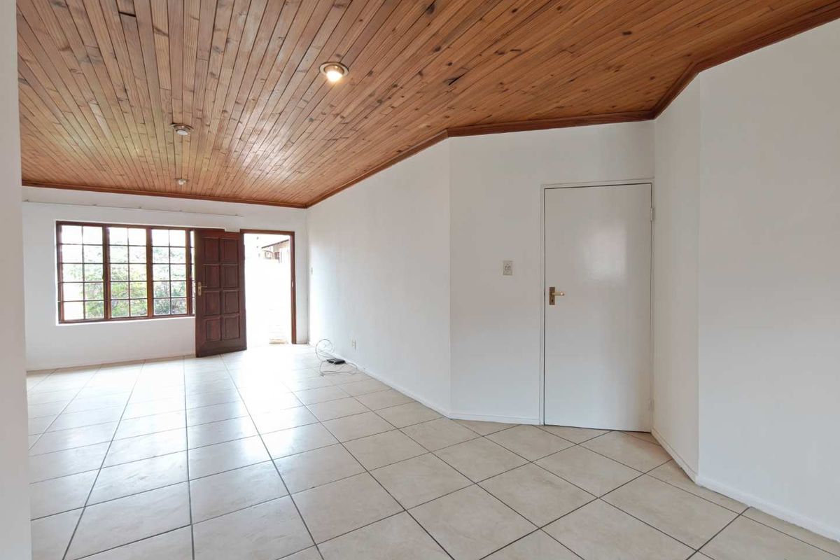 Spacious living area featuring ceramic floor tiles, a warm timber tongue and groove ceiling, and natural light through wooden window and door frames.
