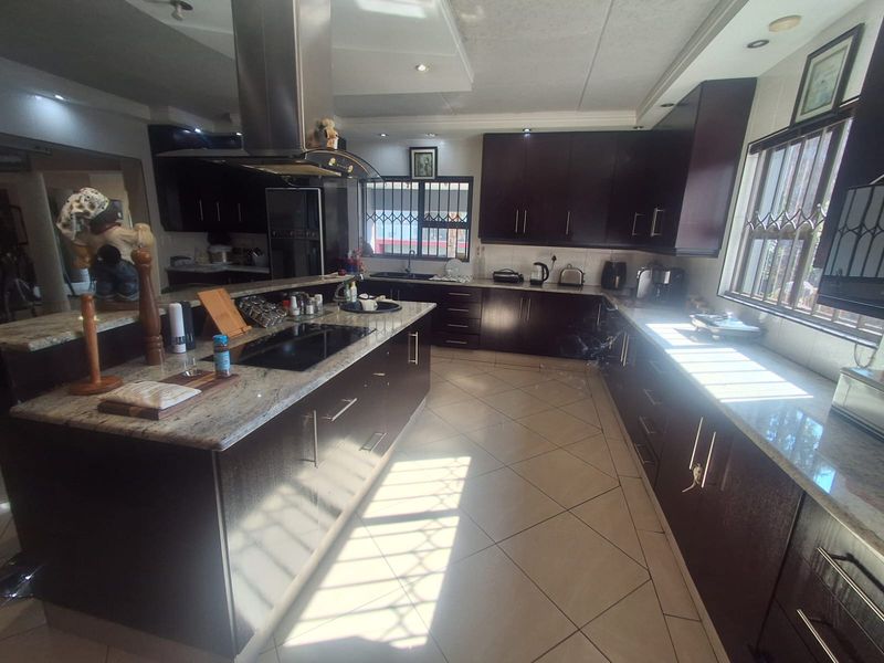 Spacious modern kitchen featuring dark wood cabinetry, granite countertops, a central island with a built-in hob, and tiled flooring throughout.