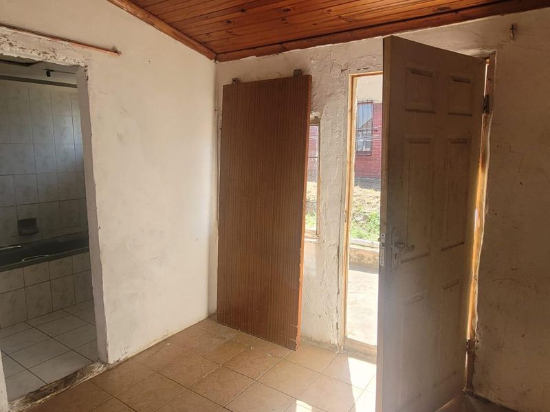 An empty bedroom featuring timber ceilings and tiled floors, requiring cosmetic renovation and wall repairs to restore its condition.