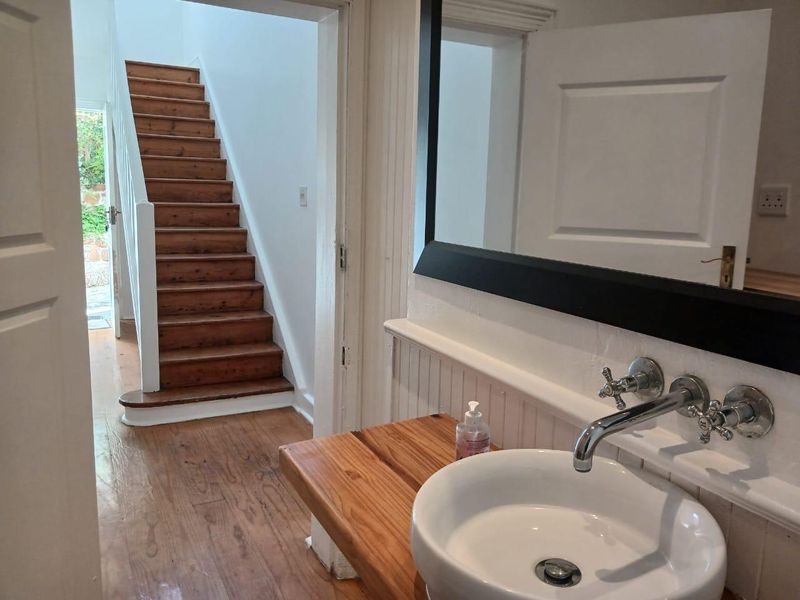 A bright bathroom featuring a vessel sink with wall-mounted hardware, timber vanity top, and beadboard wainscoting, with a view toward a timber staircase.