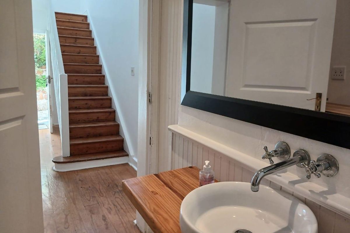 A bright bathroom featuring a vessel sink with wall-mounted hardware, timber vanity top, and beadboard wainscoting, with a view toward a timber staircase.